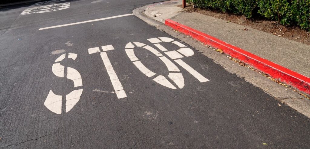 Stop Sign Painted on Asphalt of Red Curb Street at Intersection